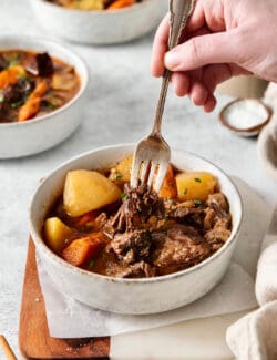 A hand holding a spoon in a bowl of goulash