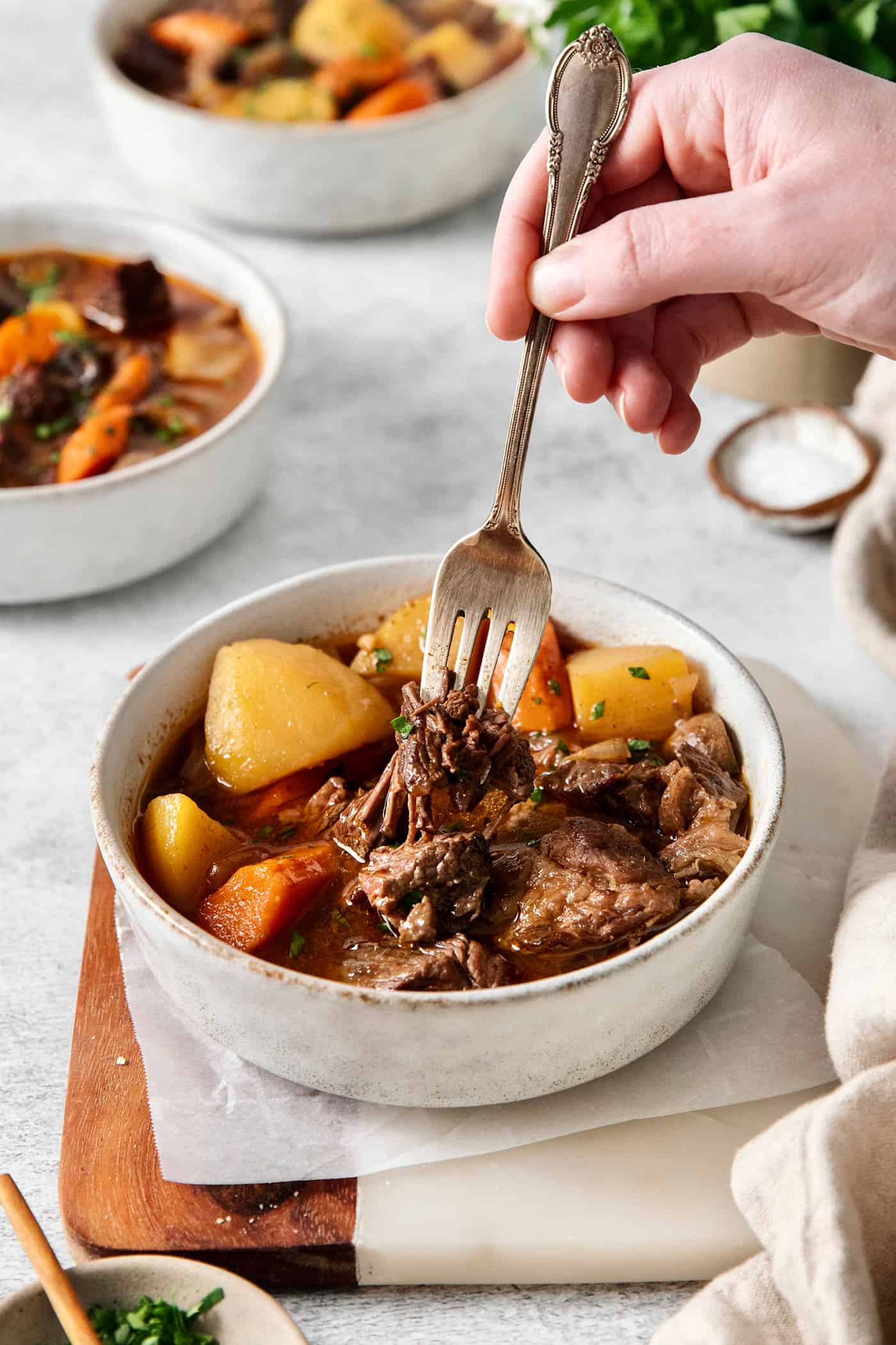 A hand holding a spoon in a bowl of goulash