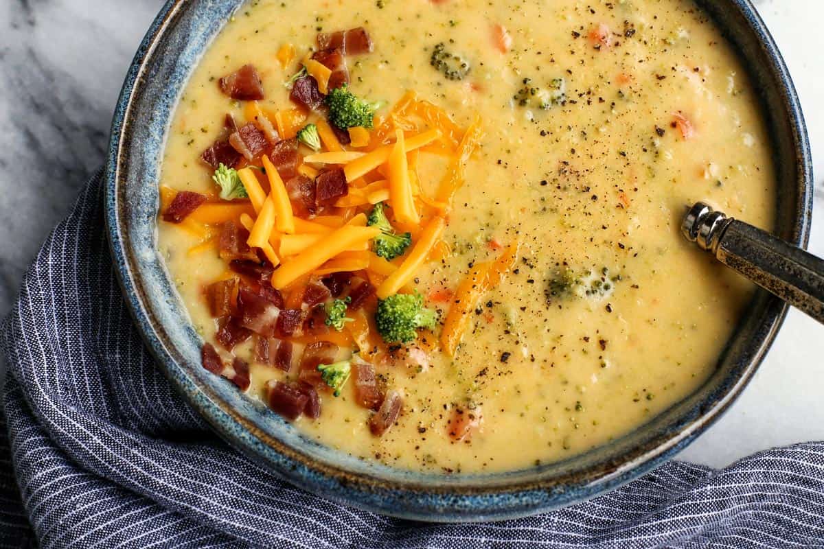 A bowl of broccoli and cheese soup topped with bacon and cheese