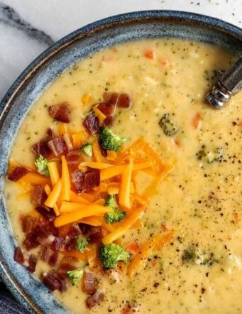 Overhead view of a bowl of broccoli cheddar soup garnished with crumbled bacon and shredded cheese.