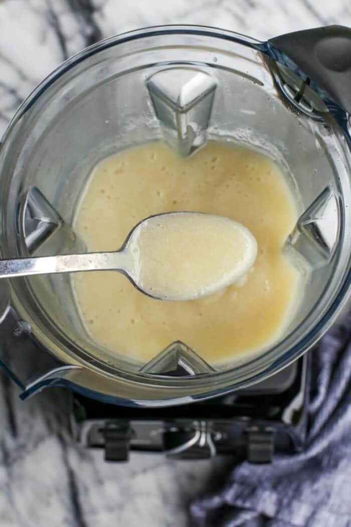 A spoonful held over blended potatoes and caulfilower in a blender.