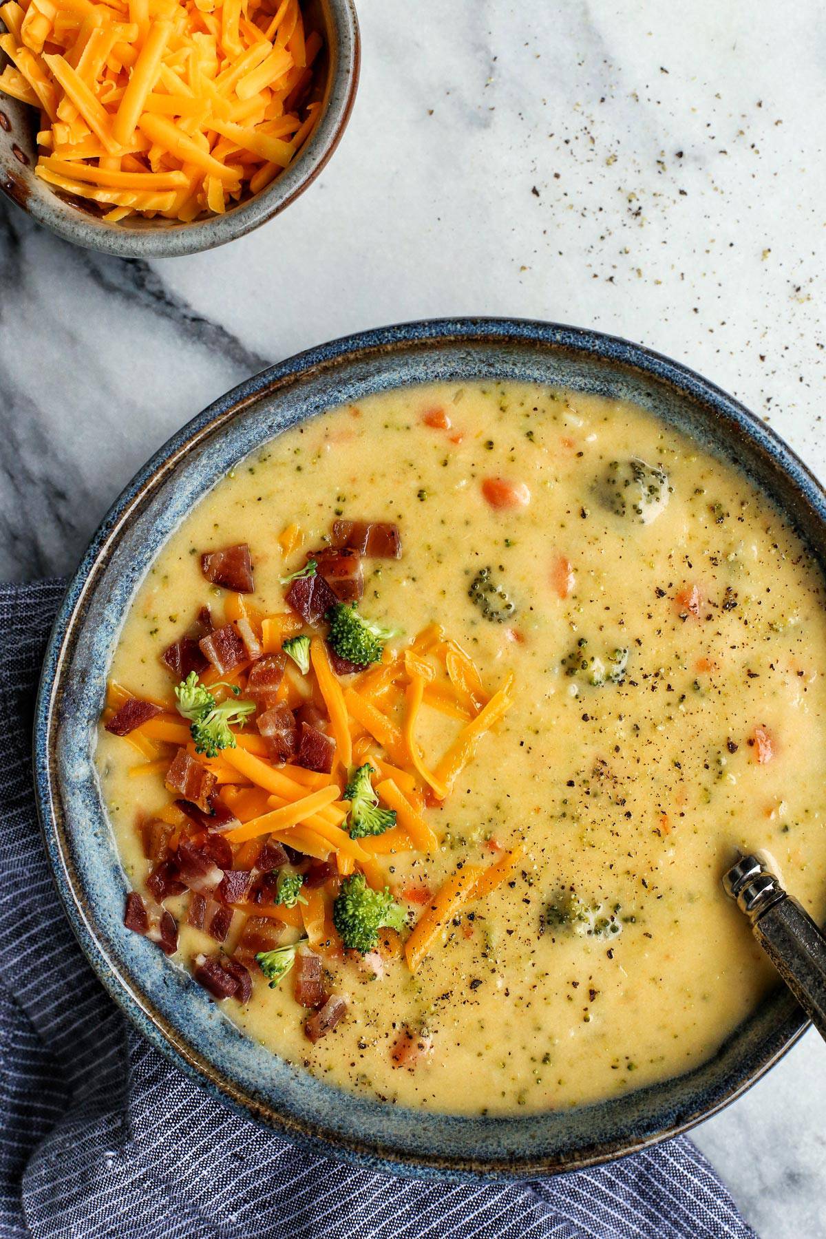 Extra cheesy and creamy, this broccoli cheddar soup recipe is loaded with all kinds of wholesome veggies. Don't forget a sprinkle of bacon! Overhead close up view of a bowl of broccoli cheddar soup garnished with crumbled bacon and shredded cheese.