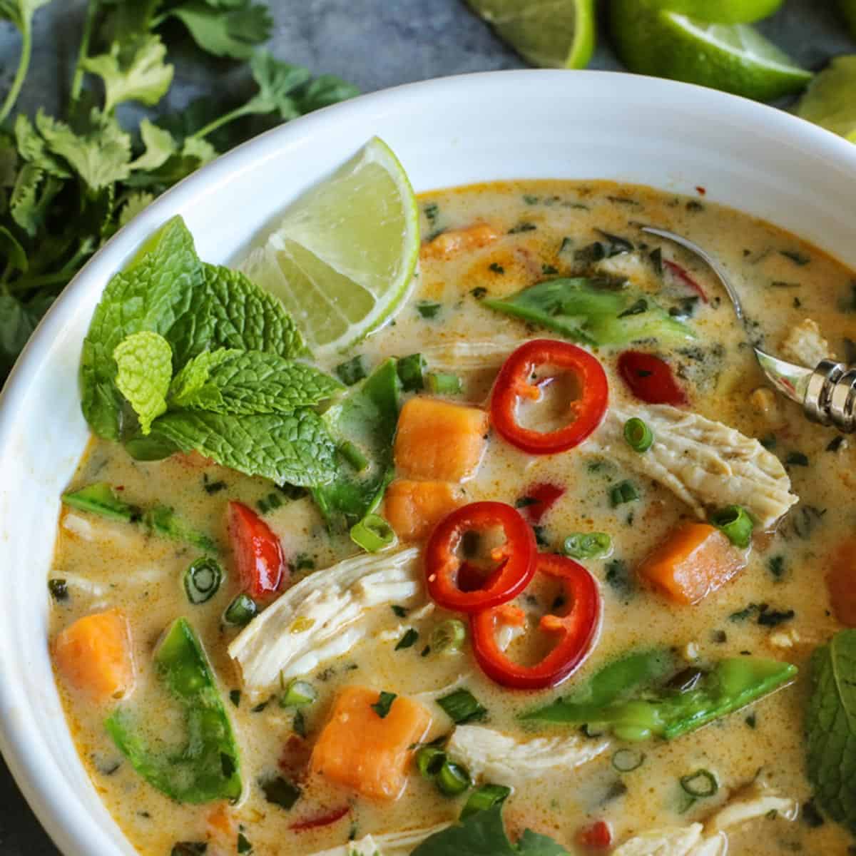 Soup with chicken and Thai flavors served in a bowl with fresh mint, lime, and peppers