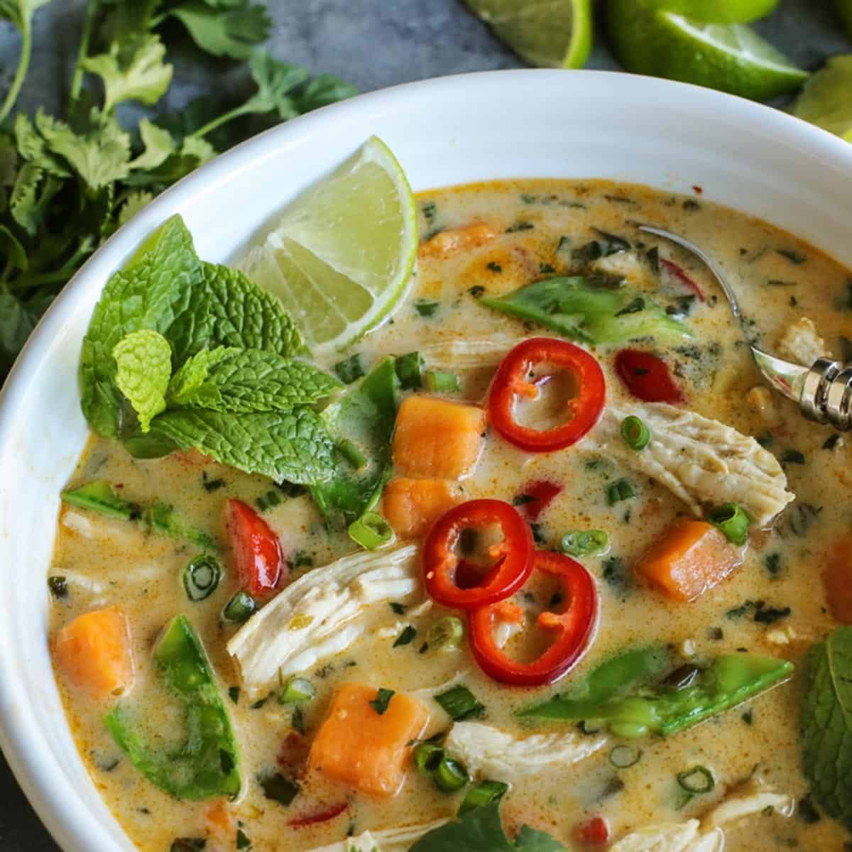 Thai Chicken Soup in a white bowl garnished with fresh mint and sliced chilies.