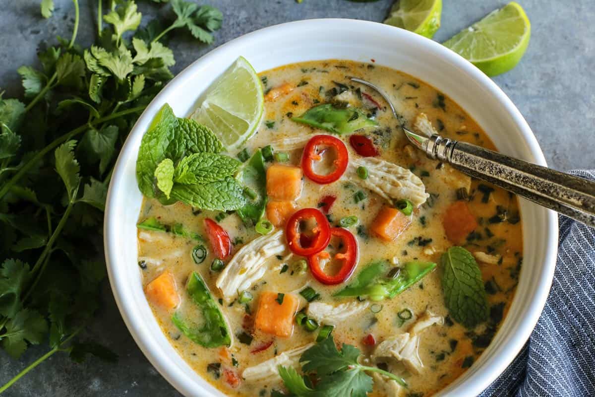 Overhead view of Thai Chicken Soup in a white bowl garnished with fresh mint and sliced chilies.