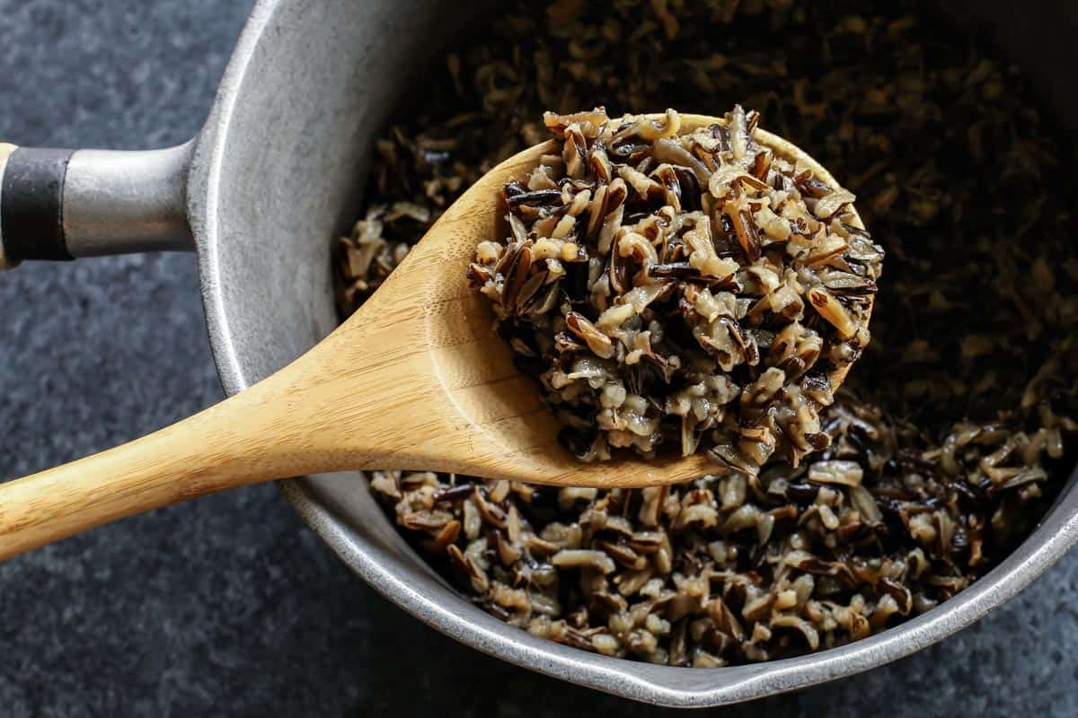 A spoonful of cooked wild rice held over a pot of rice.