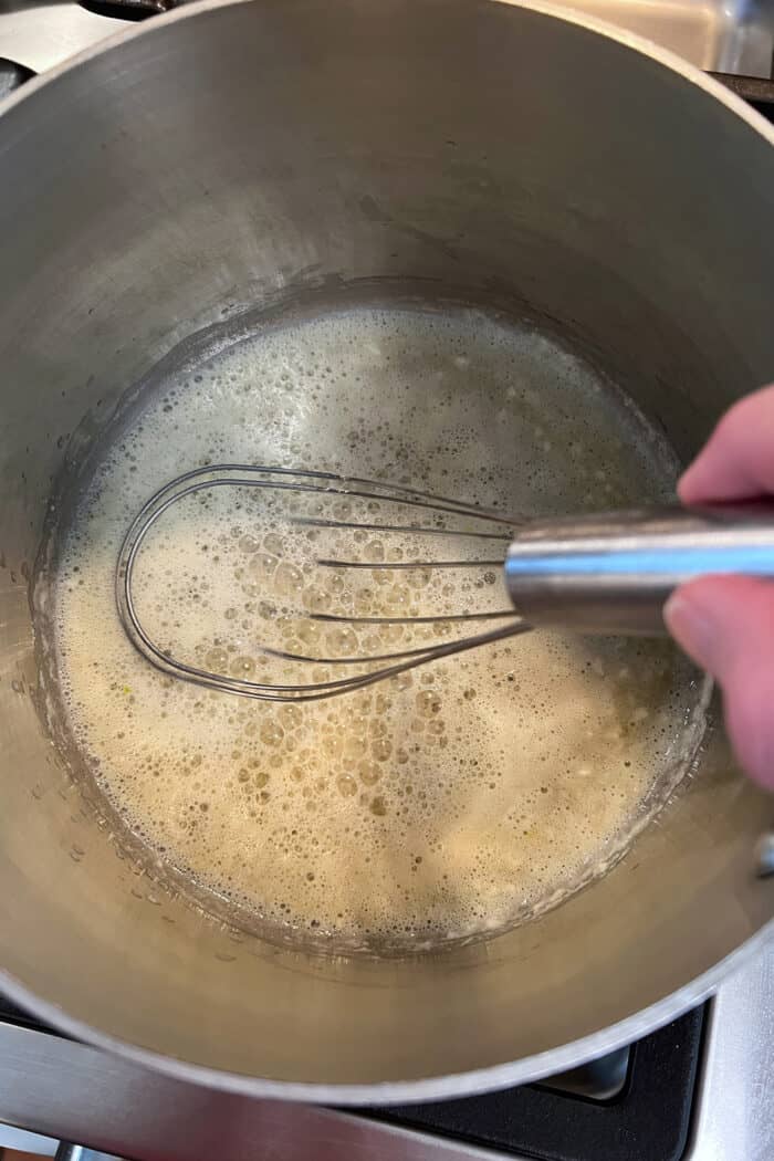 A hand whisking butter and flour in a soup pot