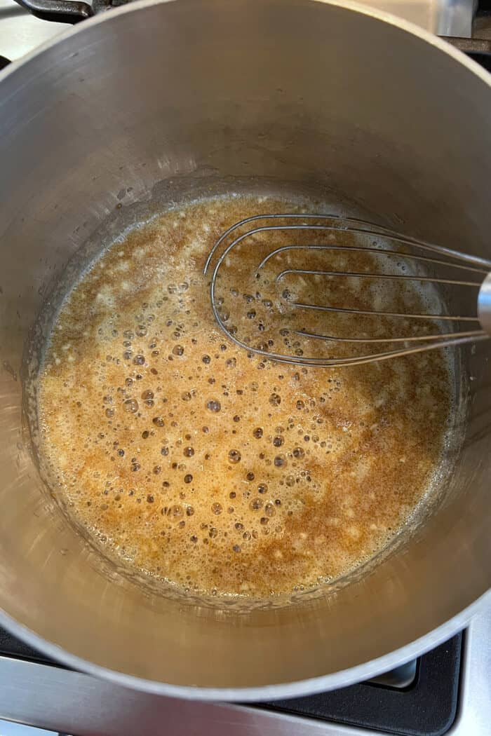 A whisk in a soup pan with simmering butter and flouring