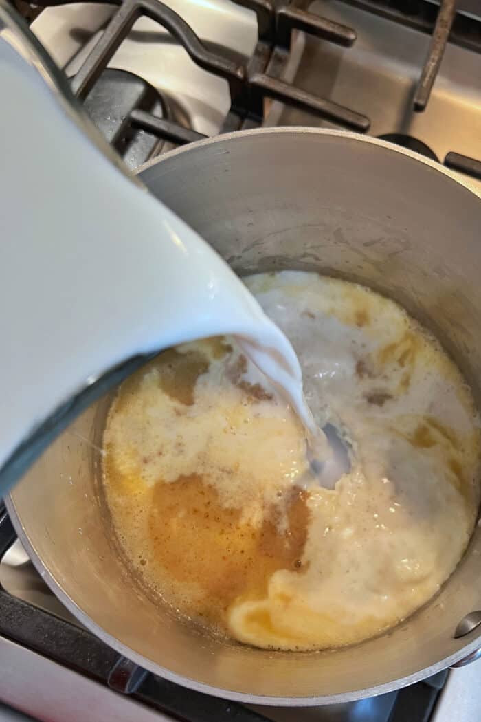 Milk being poured into a soup pan with a flour and butter mixture