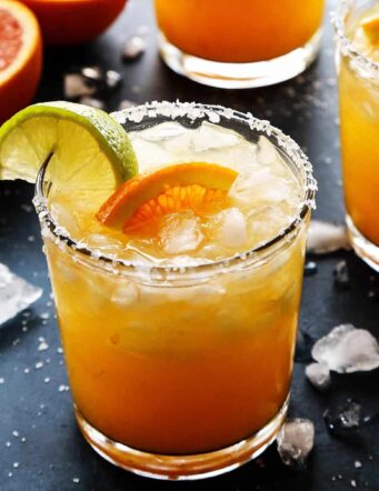 An orange margarita with fresh orange and lime wedges