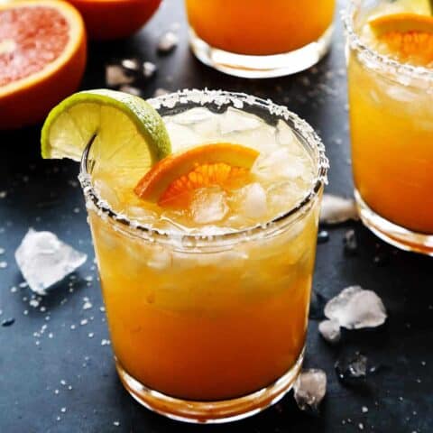 An orange margarita with fresh orange and lime wedges