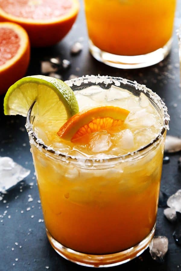 orange margarita in a glass with fresh orange and lime wedges