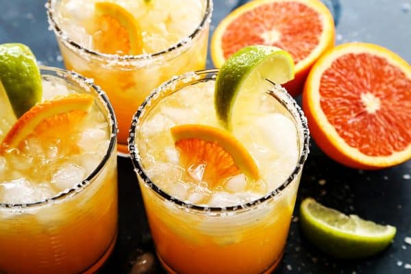 Three glasses of orange margaritas and sliced oranges