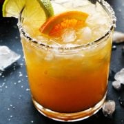 pinterest image of orange margarita in a salt-rimmed glass, with fresh orange halves