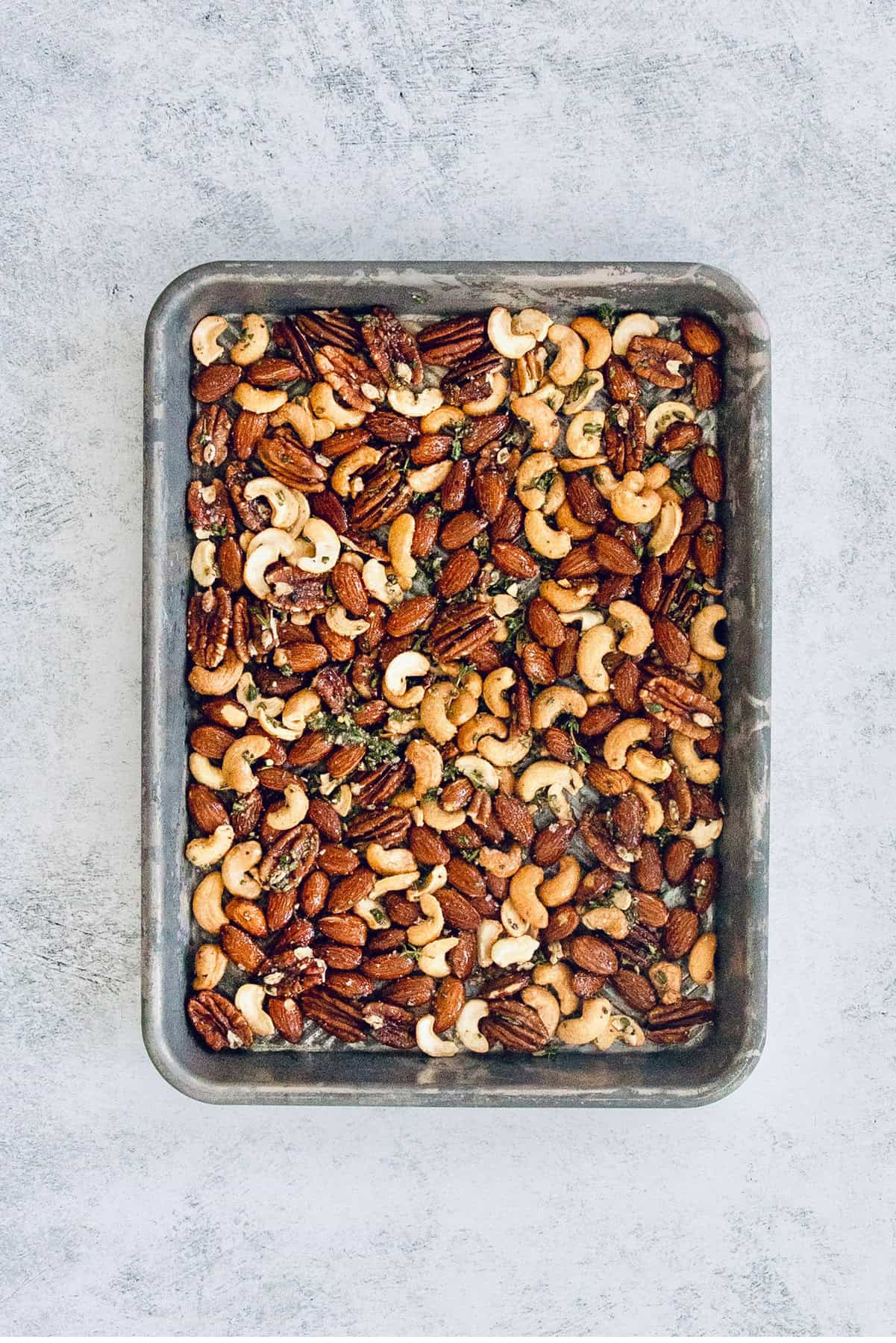 Adding the seasoned nuts to the baking tray.
