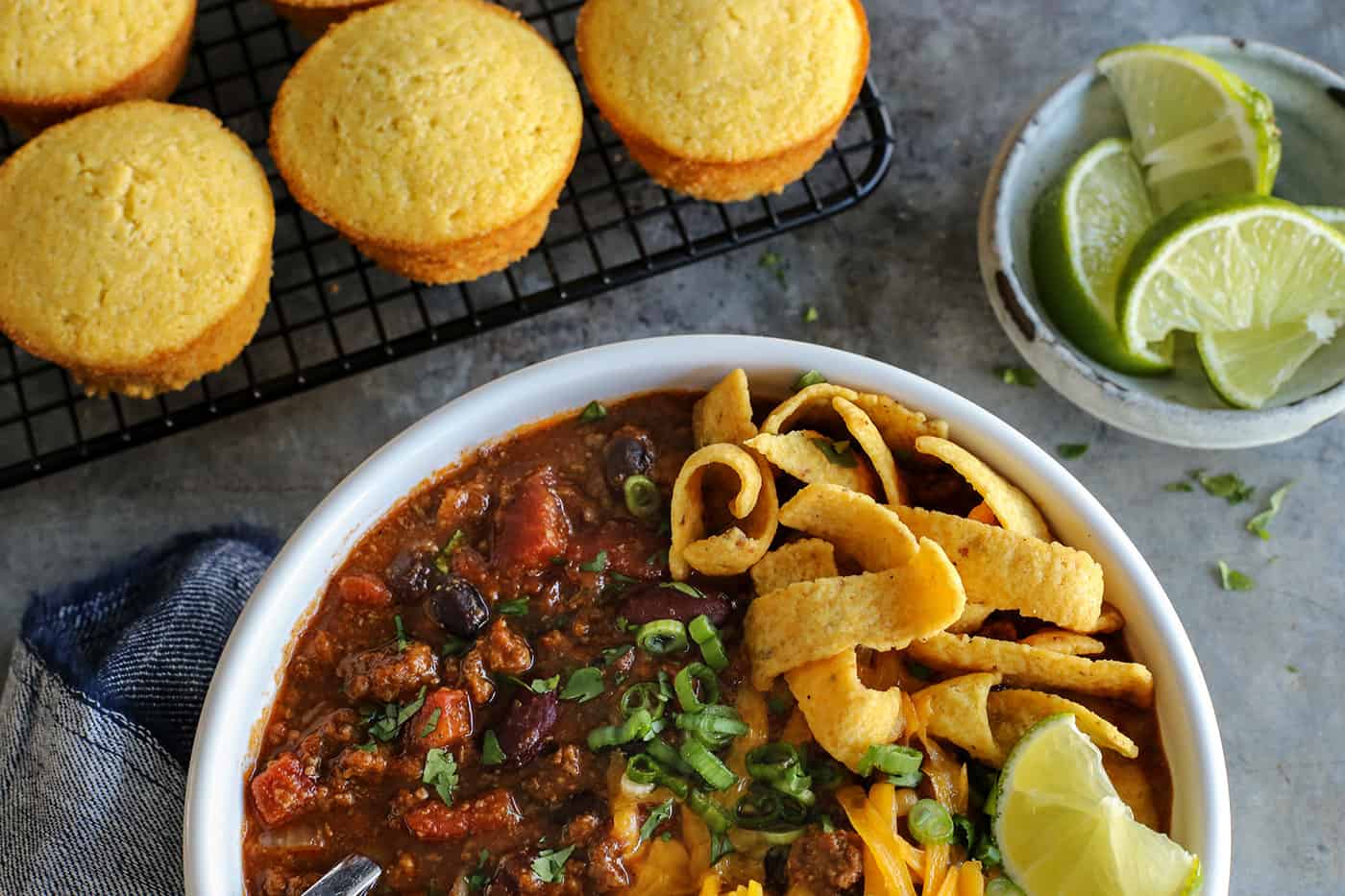 A bowl of crockpot chili with cornbread muffins in the background
