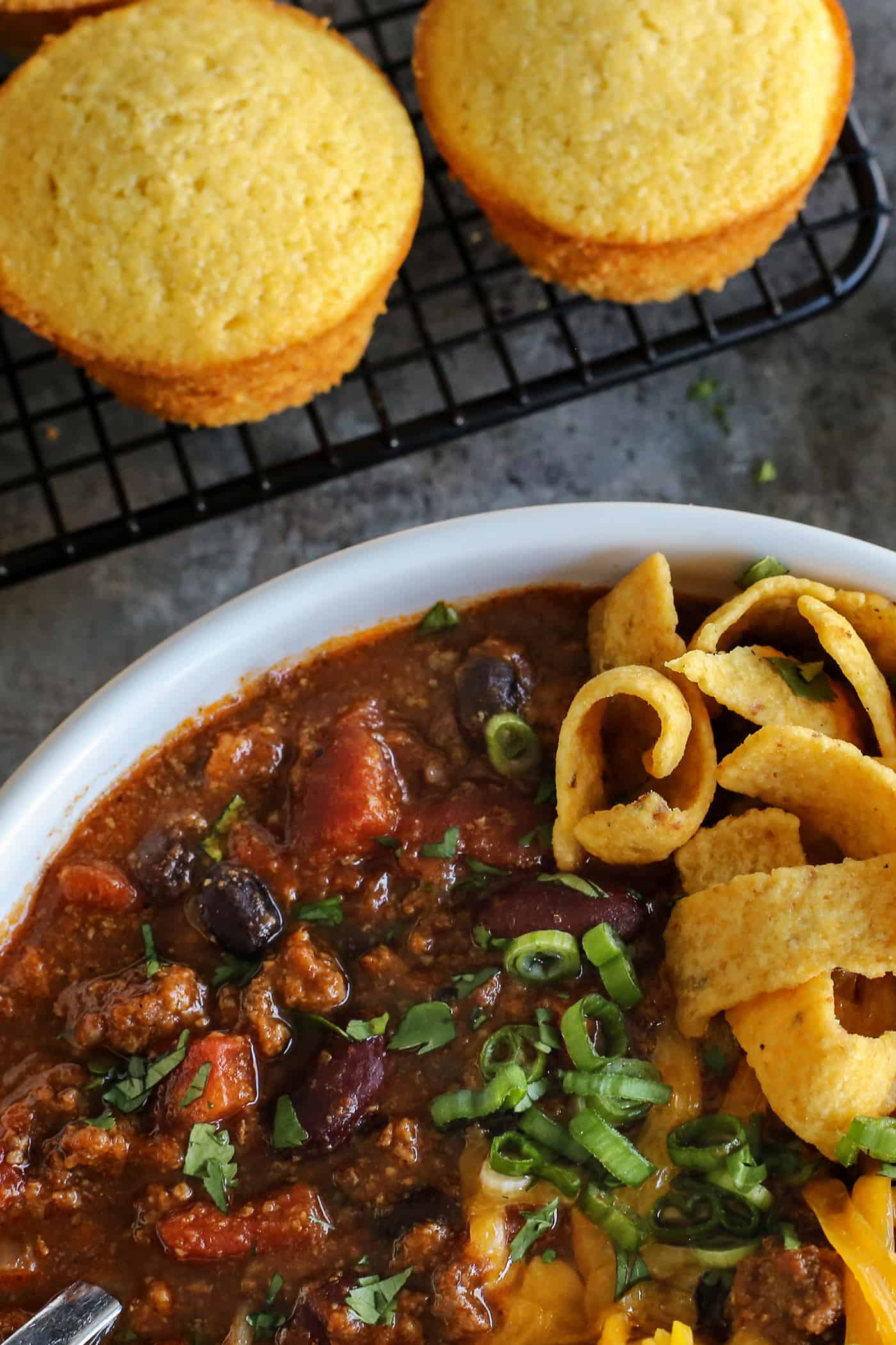 A bowl of slow cooker chili near some cornbread muffins