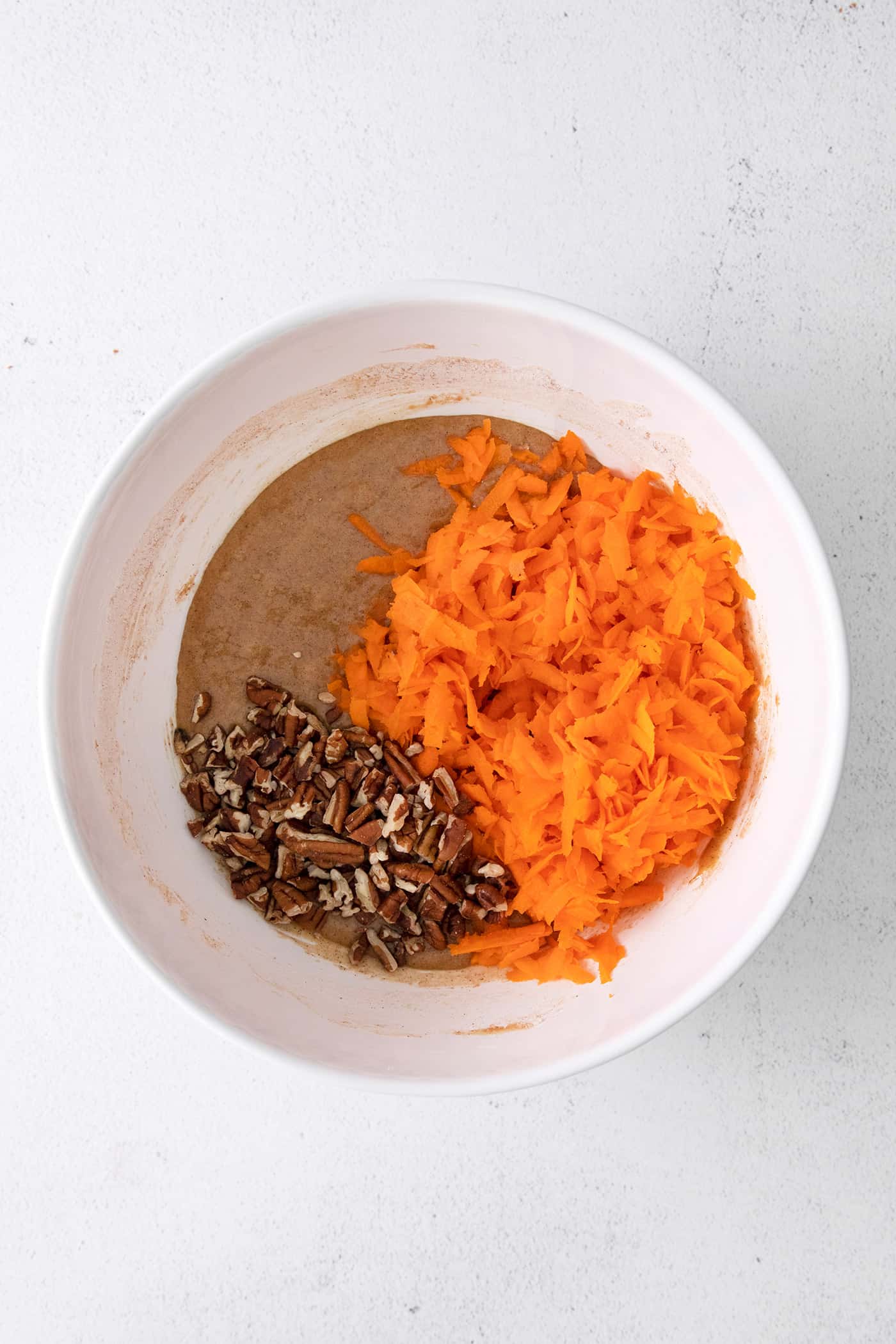 Cake batter, shredded carrots, and chopped nuts in a white bowl