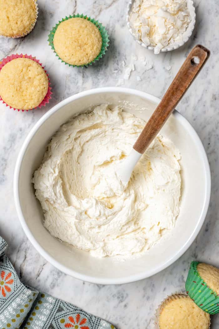 Overhead view of coconut buttercream in mixing bowl with rubber spatula