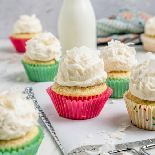 Coconut cupcakes with coconut buttercream on parchment-lined wire rack and countertop