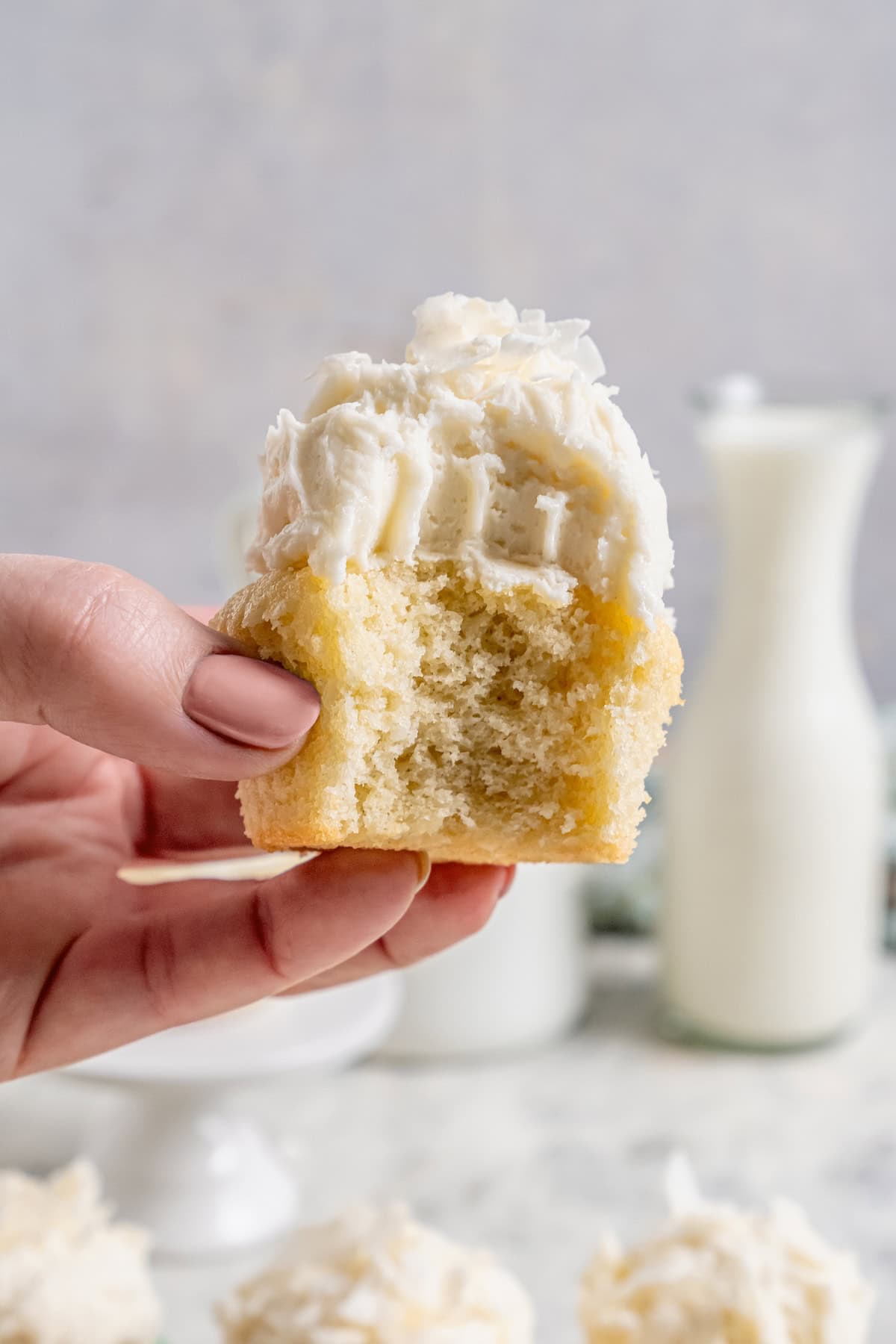 Hand holding bitten coconut cupcake, showing fluffy texture