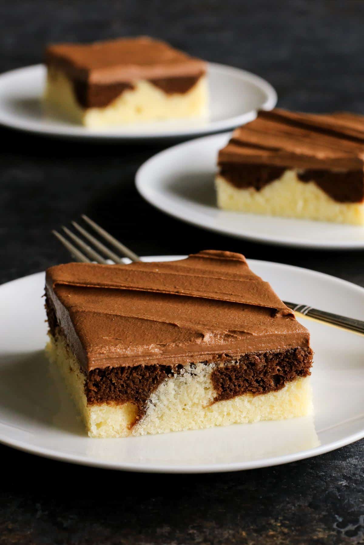 This Easy Marble Cake Recipe features a moist chocolate and vanilla sheet cake slathered with a rich & creamy chocolate buttercream frosting. three pieces of marble cake
