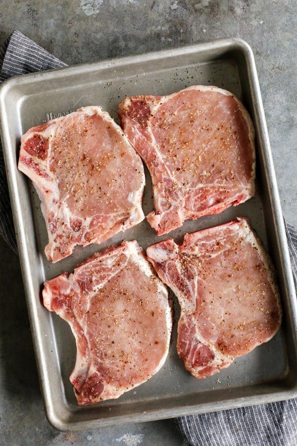 four uncooked pork chops on a pan