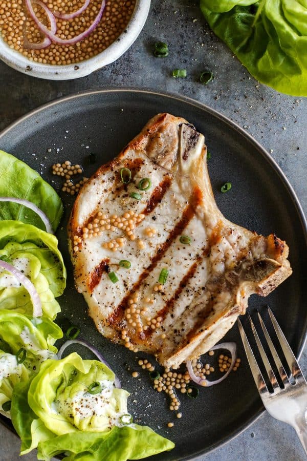 a grilled pork chop with a small side salad topped with buttermilk ranch dressing