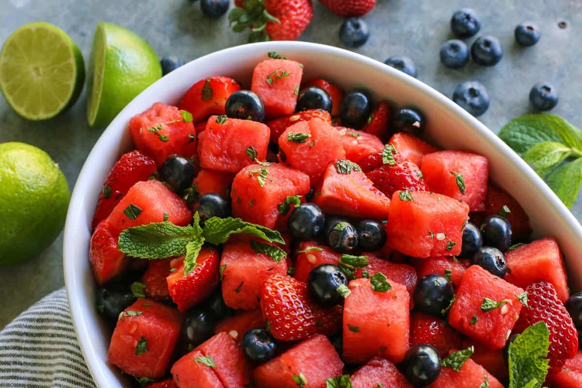 white bowl of mojito fruit salad, with fresh watermelon, strawberries, blueberries, and limes