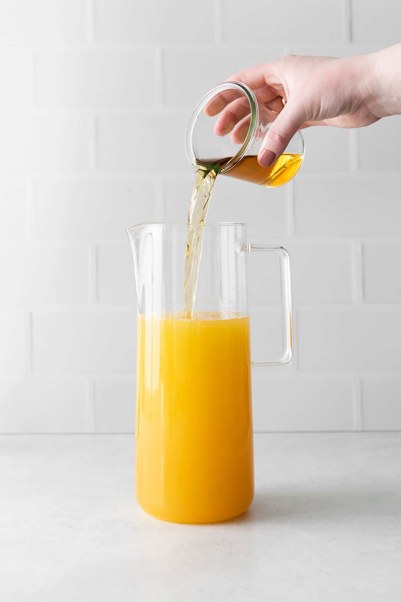 Bourbon being poured into a pitcher with pineapple juice and rum