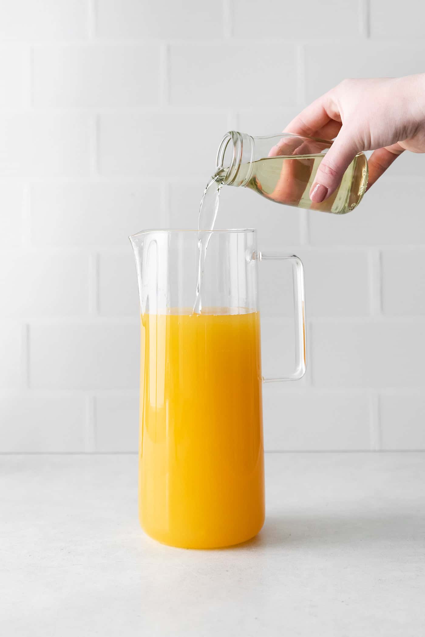 Simple syrup being added to a pitcher with wine bourbon and pineapple juice