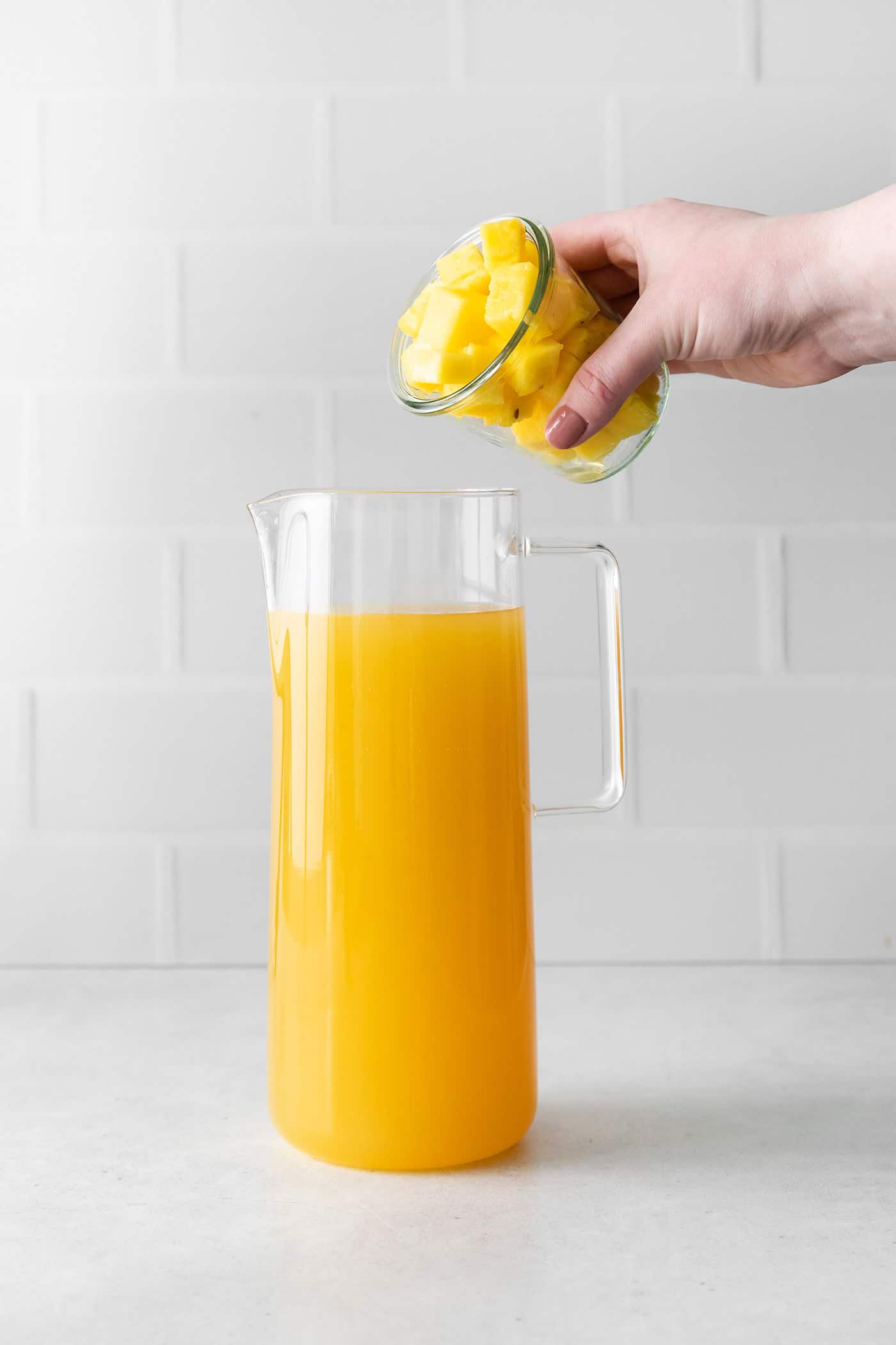 Chunks of pineapple being added to a pitcher of pineapple sangria