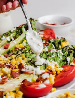Spooning buttermilk ranch dressing over salad on plate
