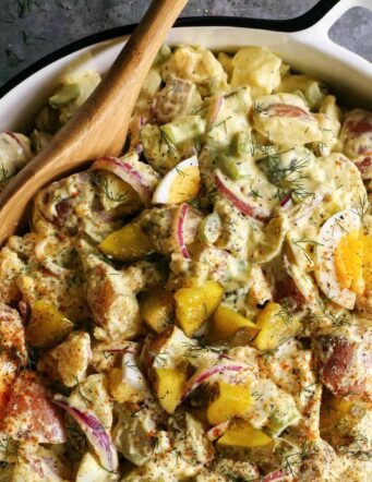 Dill potato salad in a large, white dish with a serving spoon.