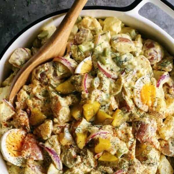 creamy salad with potatoes in a large, white dish with a serving spoon