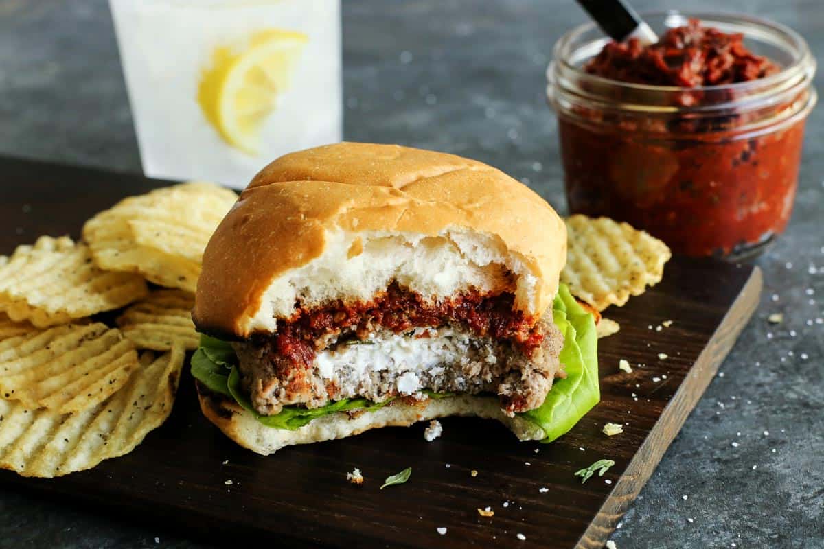 A turkey burger is served alongside chips, with a bite taken out to show the goat cheese inside.