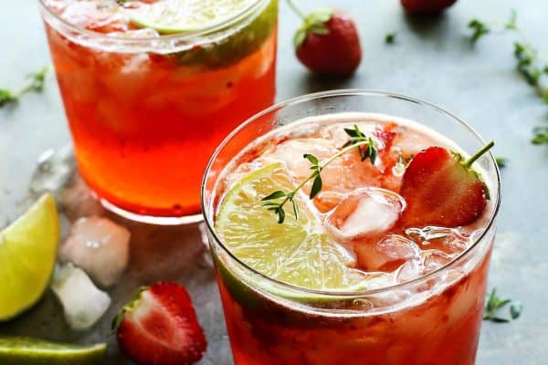 two glasses of strawberry gin and tonic with fresh strawberries and lime wedges