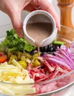 Pouring Italian vinaigrette into bowl of ingredients for Italian chopped salad