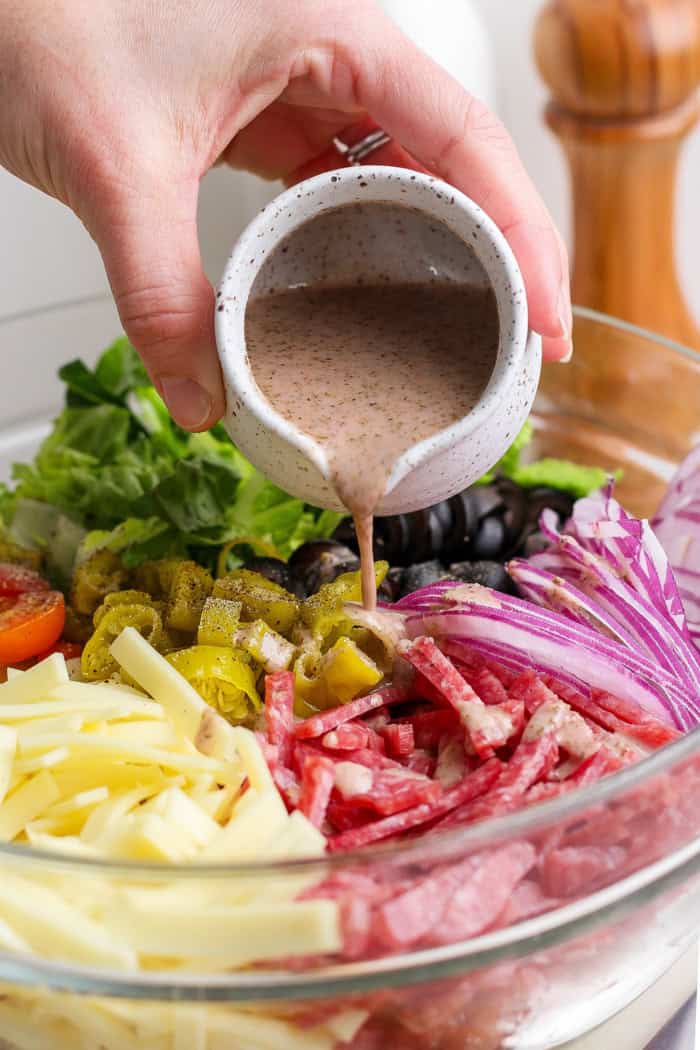 Pouring Italian vinaigrette into bowl of ingredients for Italian chopped salad