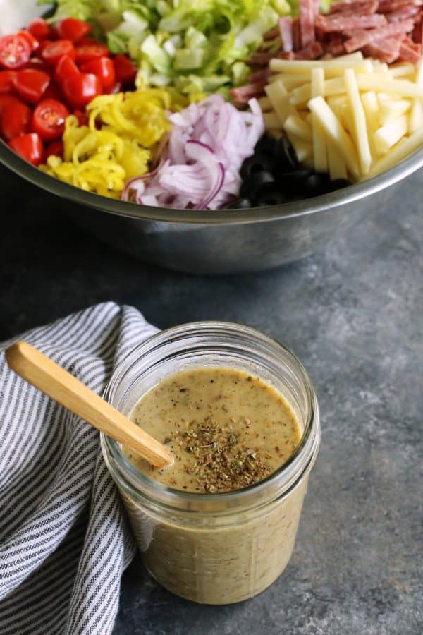 jar of Italian salad dressing and large stainless steel bowl of Italian salad in the background