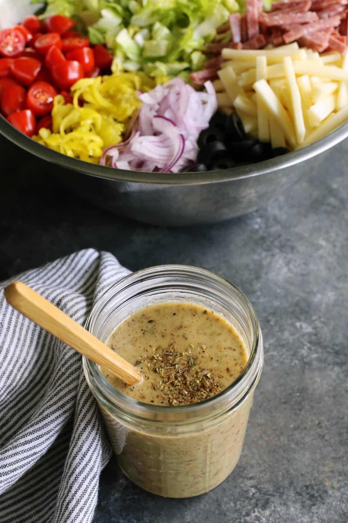 jar of Italian salad dressing and large stainless steel bowl of Italian salad in the background