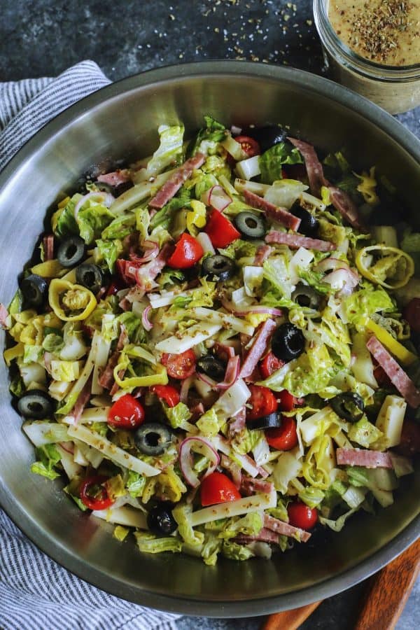 Italian chopped salad in a large stainless steel bowl, with a jar of Italian vinaigrette 