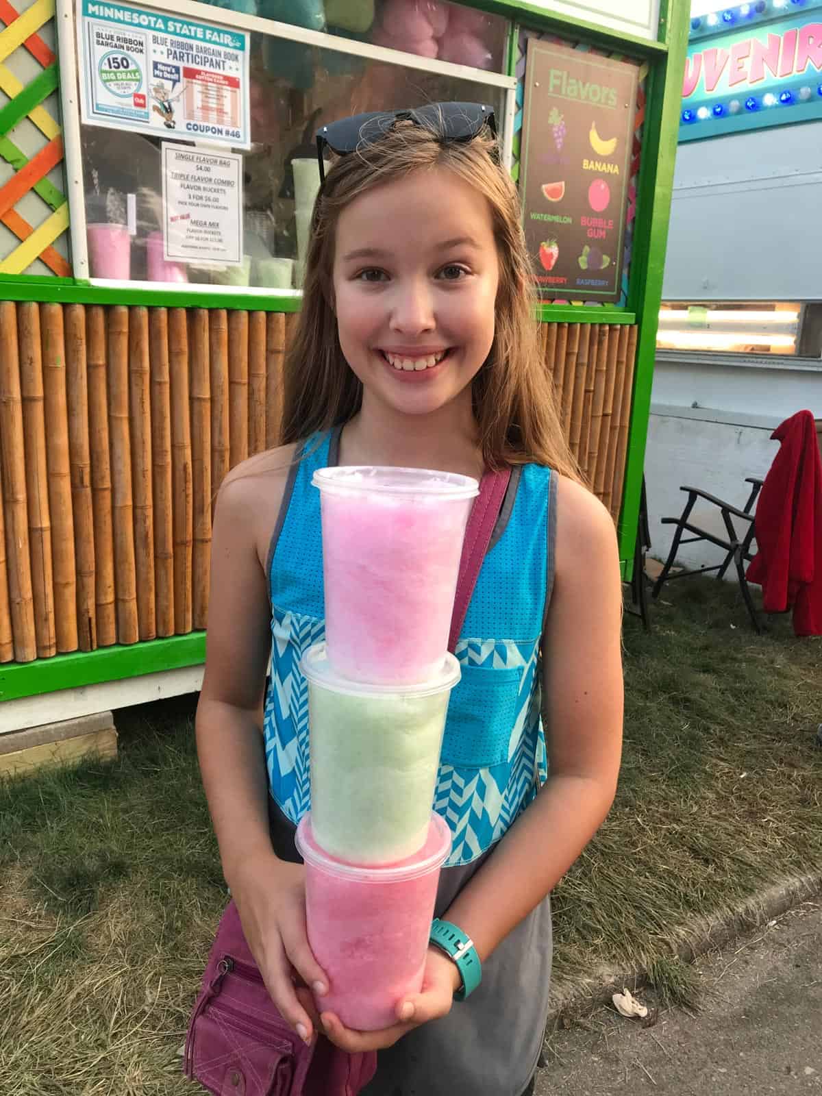 girl holding a stack of 3 containers with different flavors of cotton candy