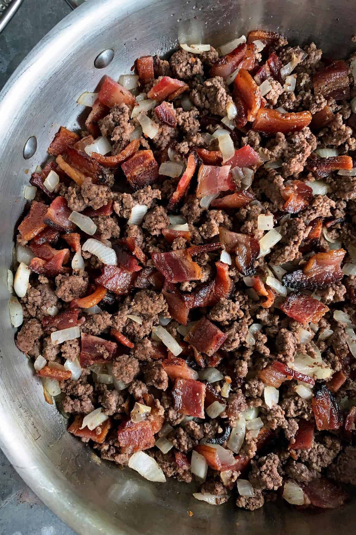 skillet of browned ground beef, bacon pieces, and chopped onion