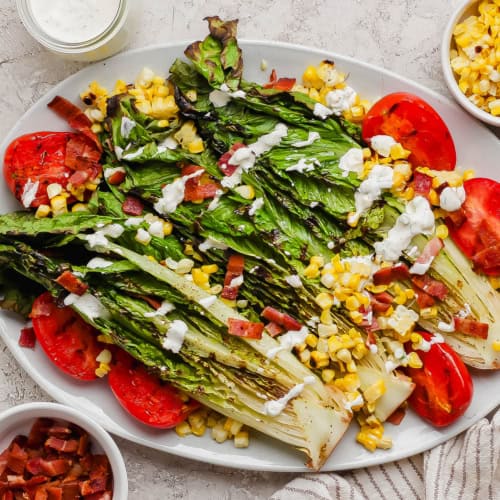 Overhead view of grilled romaine salad on platter with grilled tomatoes and corn