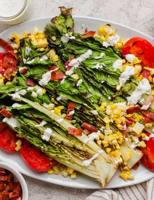 Overhead view of grilled romaine salad on platter with grilled tomatoes and corn