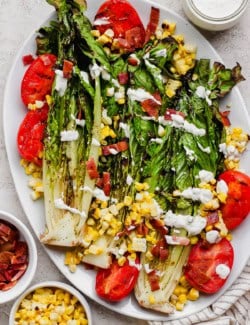 Overhead view of grilled romaine salad on platter with grilled tomatoes and corn