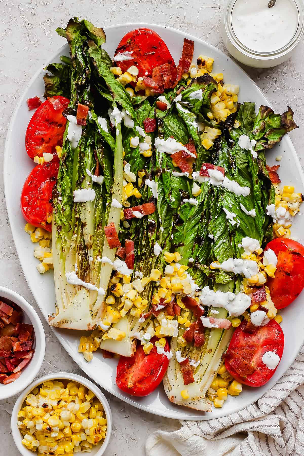 This smoky Grilled Romaine Salad is simple and summery, with tomatoes, sweet corn, crispy bacon and homemade buttermilk ranch dressing. Yum! Overhead view of grilled romaine salad on platter with grilled tomatoes and corn