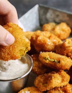 a hand dipping a fried pickle slice into ranch dip