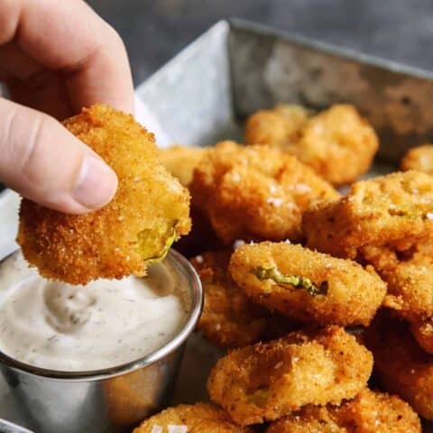 a hand dipping a fried pickle slice into ranch dip